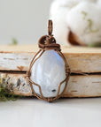 Front view of natural polished-raw rainbow moonstone pendant showing subtle flash and antique bronze copper wire wrapping