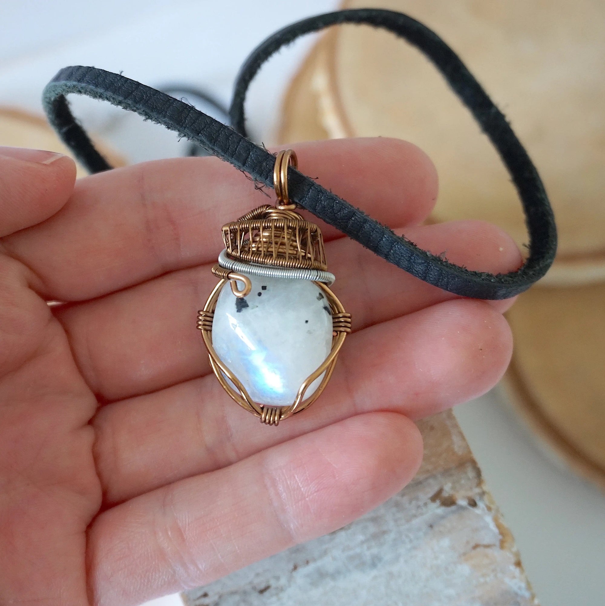 Rainbow moonstone pendant shown in hand for size reference with mixed metal artisan wire wrapping for men