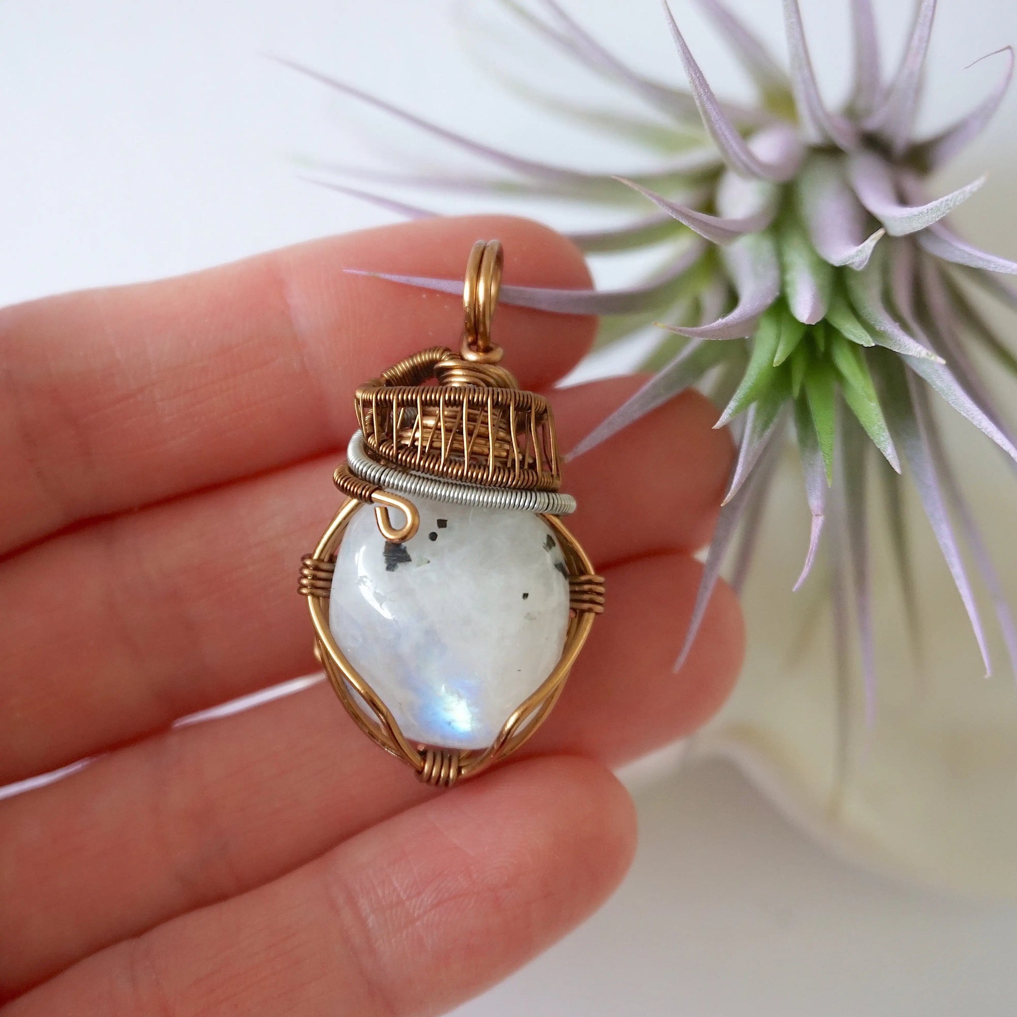 Rainbow moonstone pendant shown in hand for size reference with mixed metal artisan wire wrapping