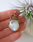 Rainbow moonstone pendant shown in hand for size reference with mixed metal artisan wire wrapping