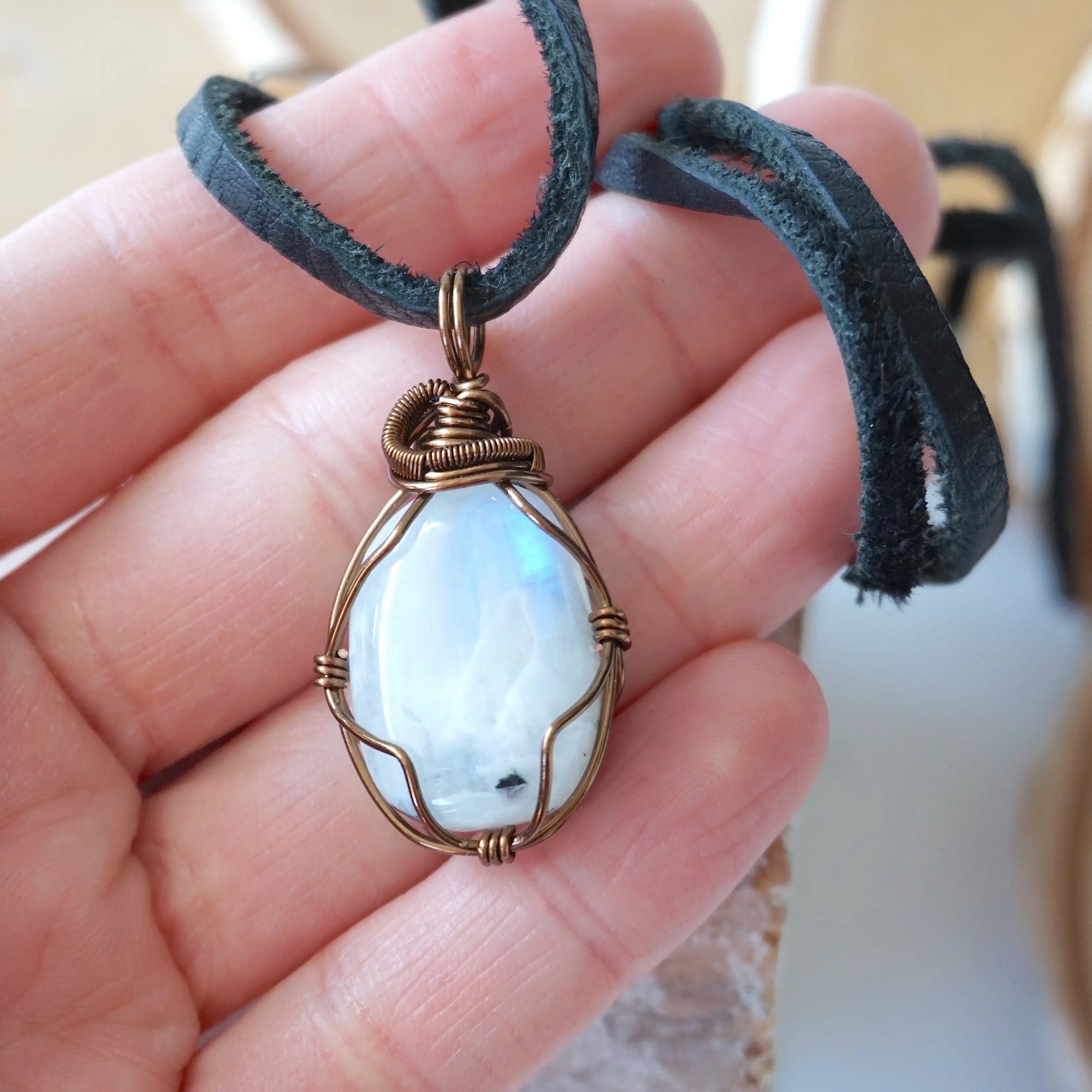 Natural rainbow moonstone pendant shown in hand for size reference with handcrafted antique bronze wire wrapping for men