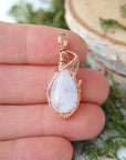 Rainbow moonstone cabochon pendant shown in hand for size reference with handcrafted 14k rose gold filled wire wrap