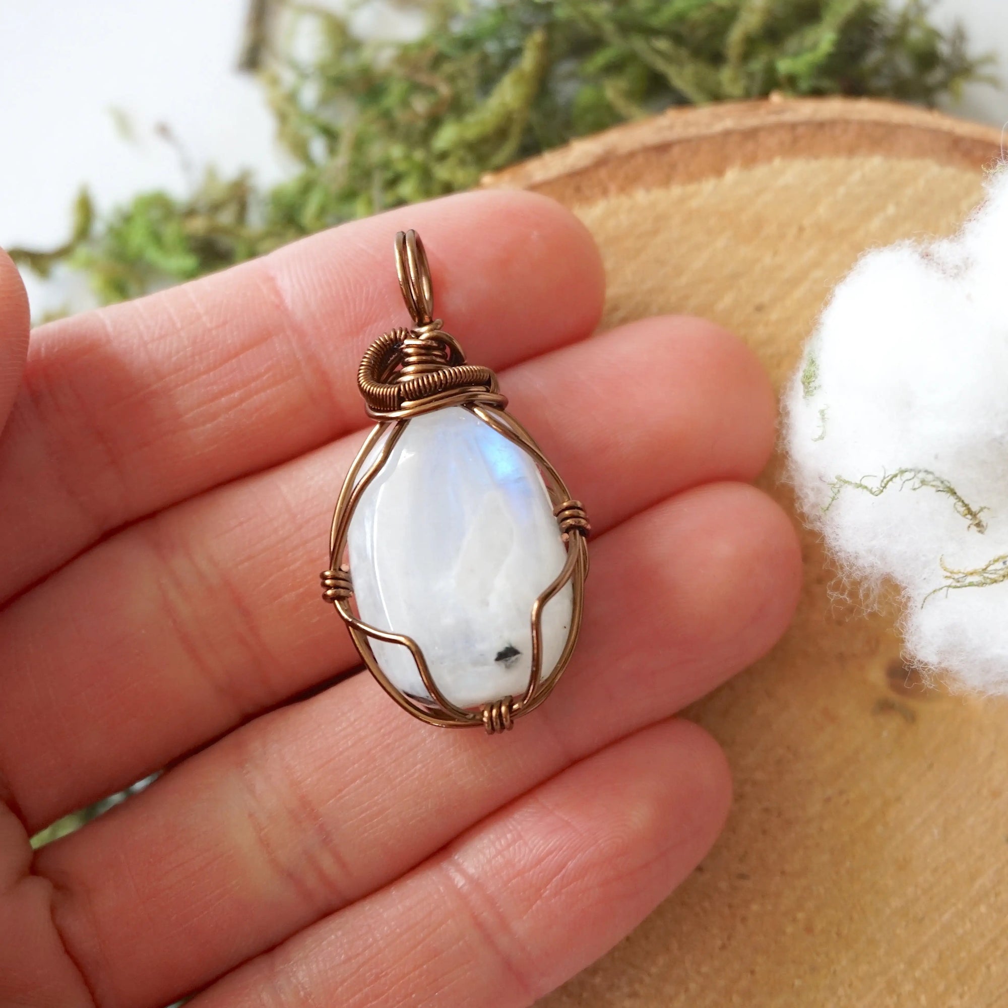 Natural rainbow moonstone pendant shown in hand for size reference with handcrafted antique bronze finish over copper wire wrapping
