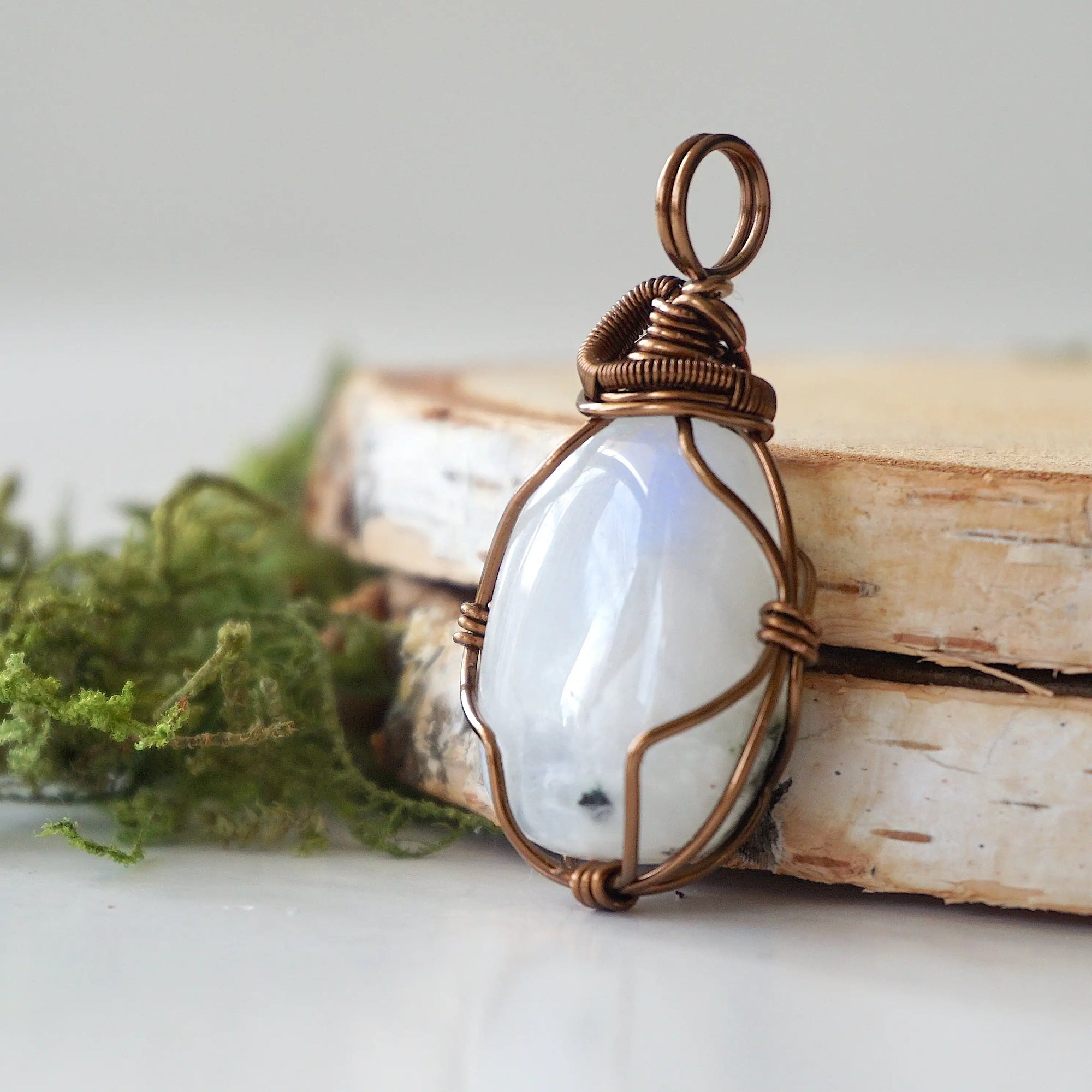 Left angle close-up of rainbow moonstone pendant showing handcrafted antique bronze copper wire wrapping and natural stone detail