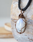 Left angle close-up of natural rainbow moonstone pendant highlighting artisan antique bronze copper wire wrapping