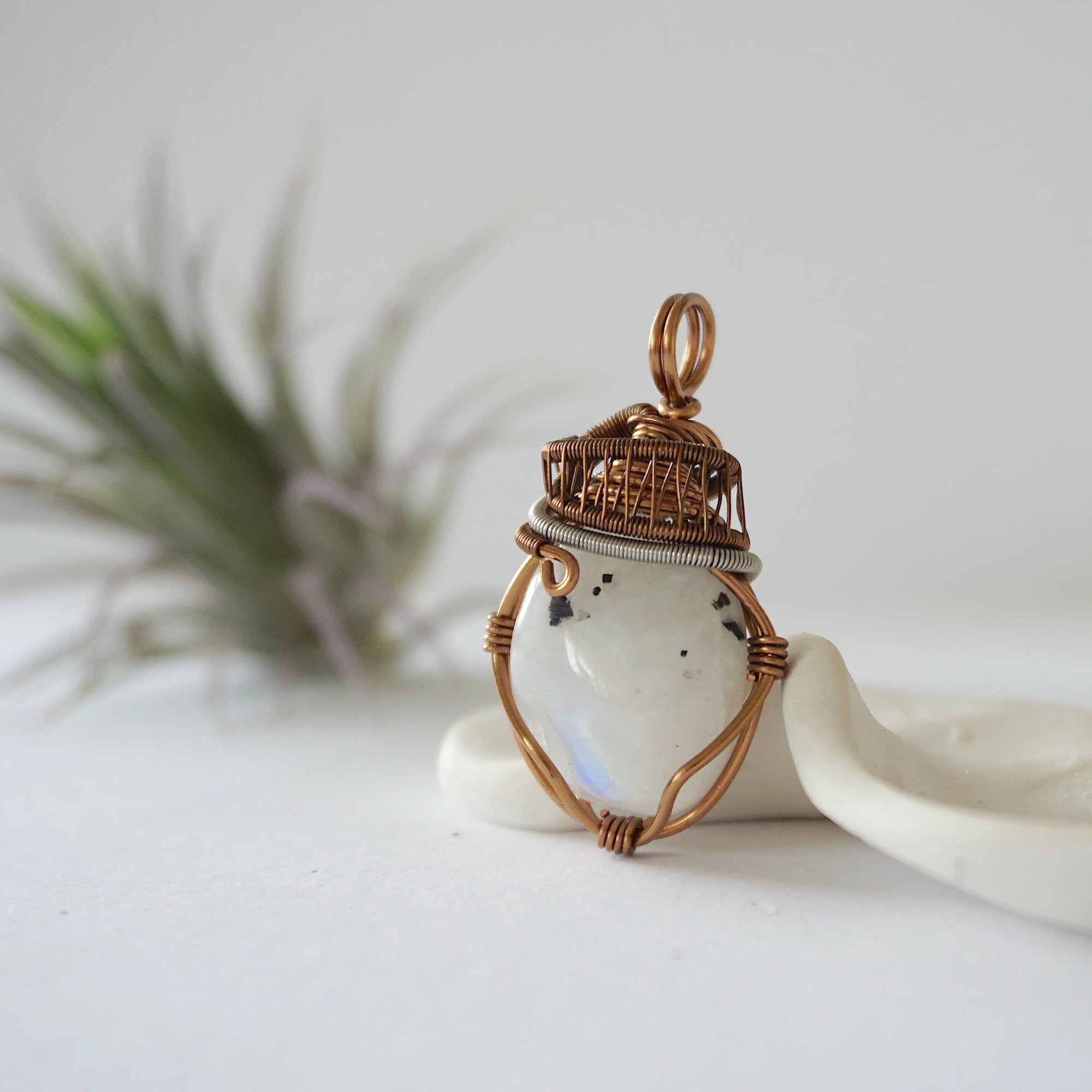 Left angle view of natural rainbow moonstone pendant highlighting artisan antique bronze and dark silver wire wrapping