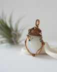 Left angle view of natural rainbow moonstone pendant highlighting artisan antique bronze and dark silver wire wrapping