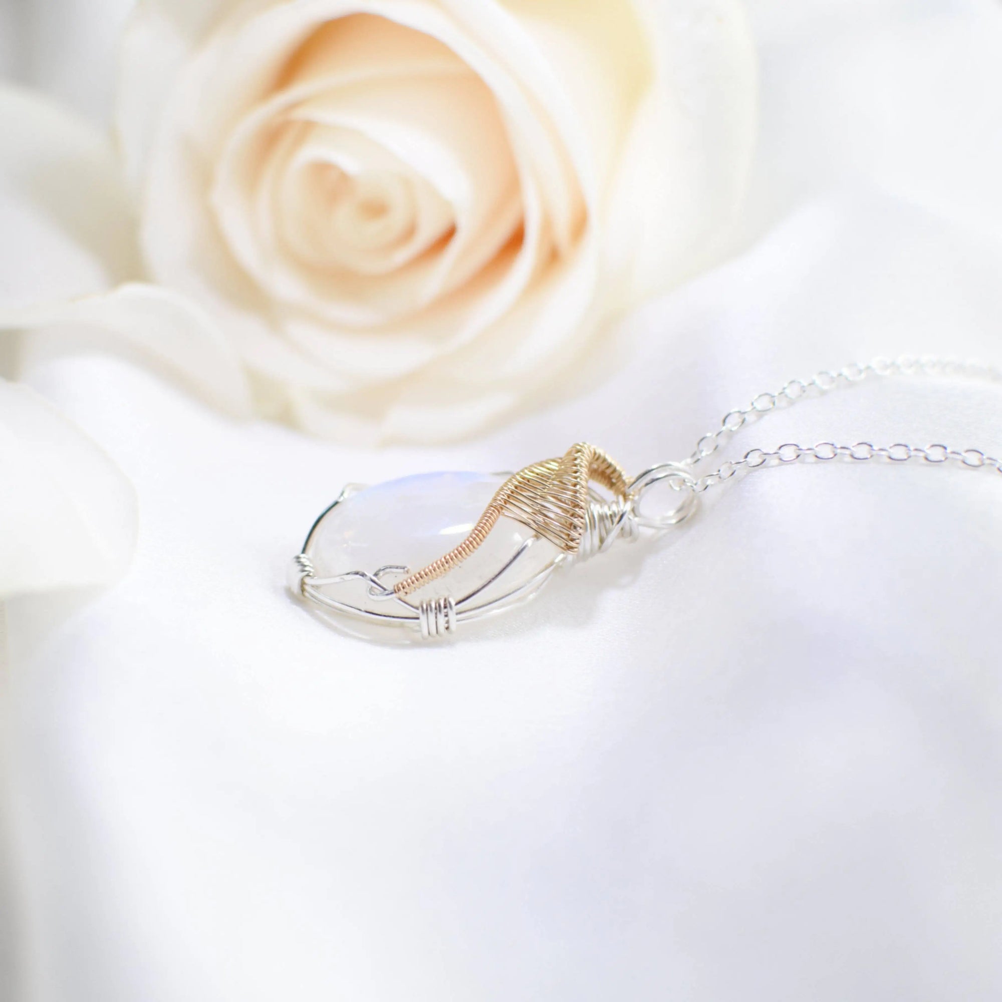 Left angle close-up of rainbow moonstone cabochon pendant with sterling silver and 14k gold filled wire wrap detail.
