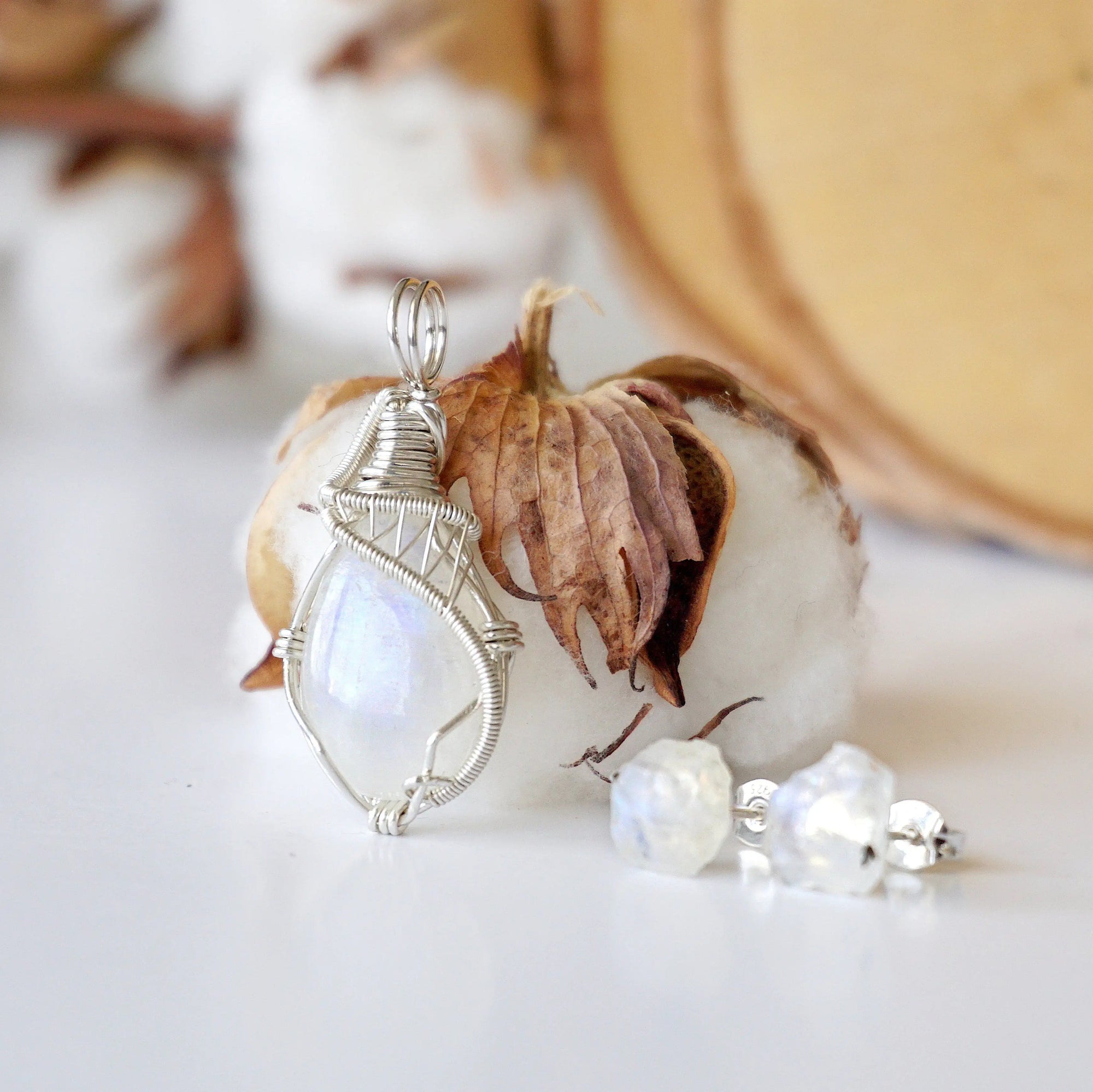 Left angle close-up of sterling silver wire wrapped rainbow moonstone cabochon pendant with matching raw moonstone stud earrings.
