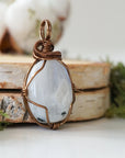 Right angle close-up of rainbow moonstone pendant highlighting detailed artisan antique bronze finish over copper wire wrapping