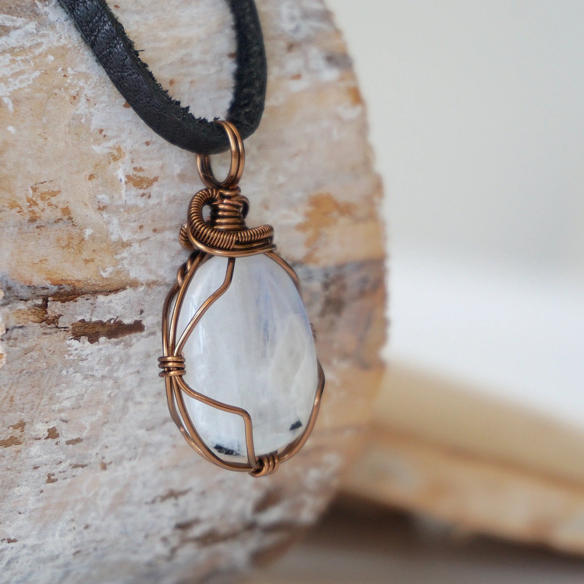 Right angle close-up of rainbow moonstone pendant showing detailed antique bronze finish over copper wire wrapping