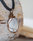 Right angle close-up of rainbow moonstone pendant showing detailed antique bronze finish over copper wire wrapping