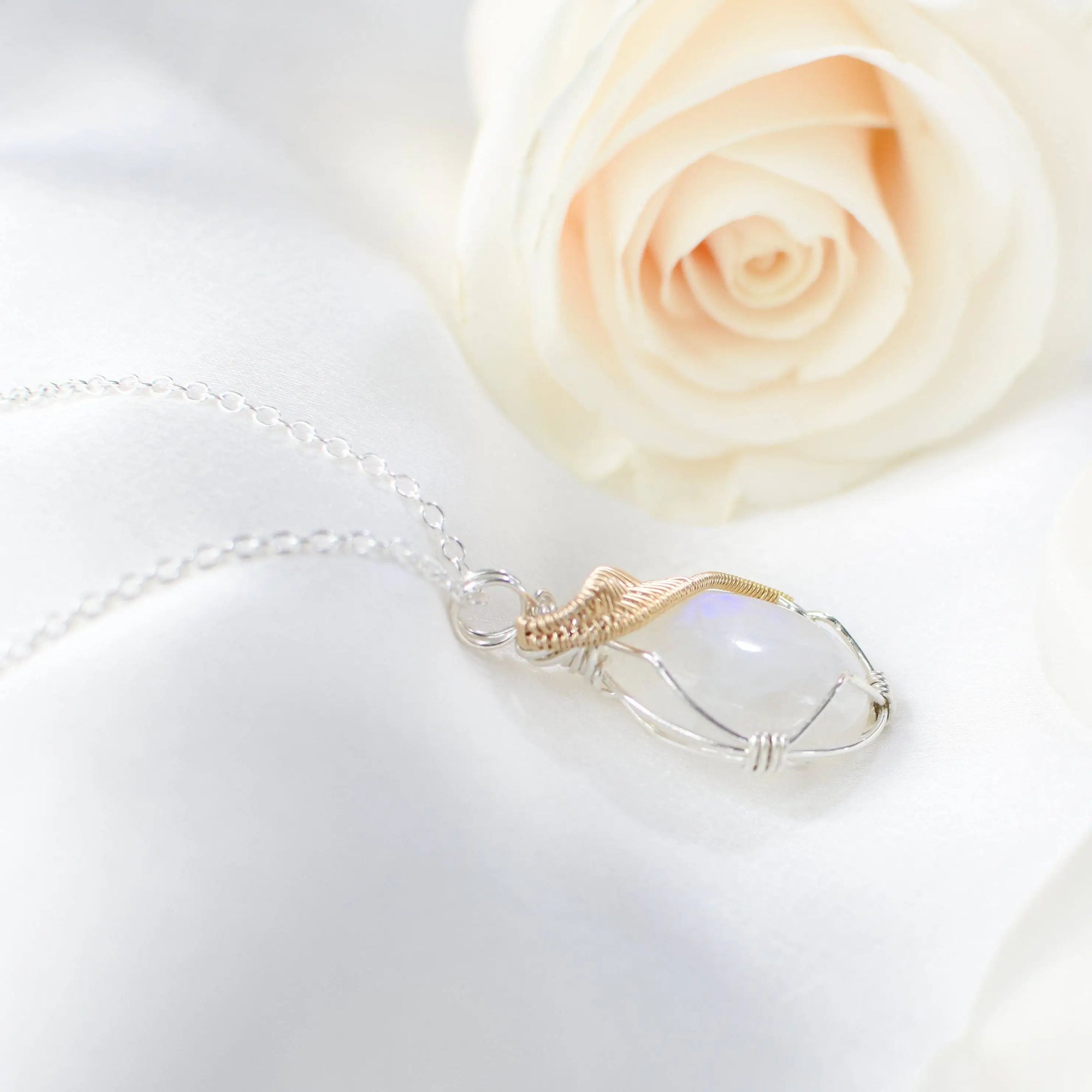 Right angle close-up of natural rainbow moonstone cabochon pendant with mixed sterling silver and 14k gold filled wire wrapping.