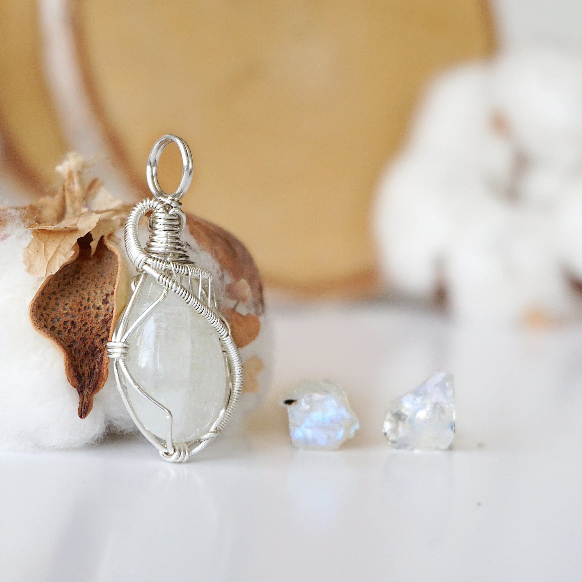 Right angle close-up of sterling silver wire wrapped rainbow moonstone cabochon pendant with matching raw moonstone stud earrings.