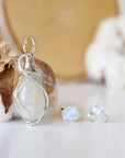 Right angle close-up of sterling silver wire wrapped rainbow moonstone cabochon pendant with matching raw moonstone stud earrings.