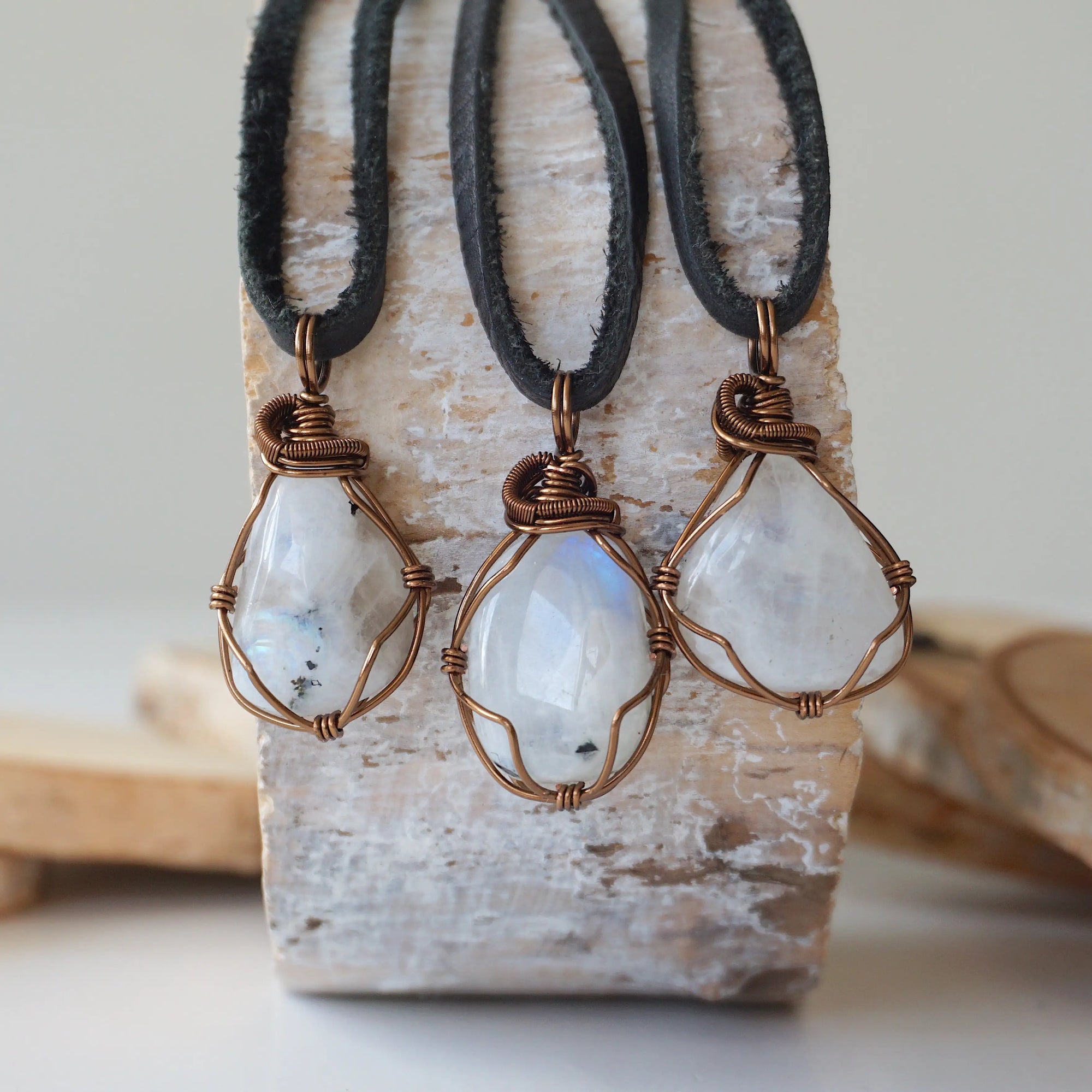 Three natural rainbow moonstone pendants showing variation in size, shape and colour shade in handmade wire wrapped jewelry