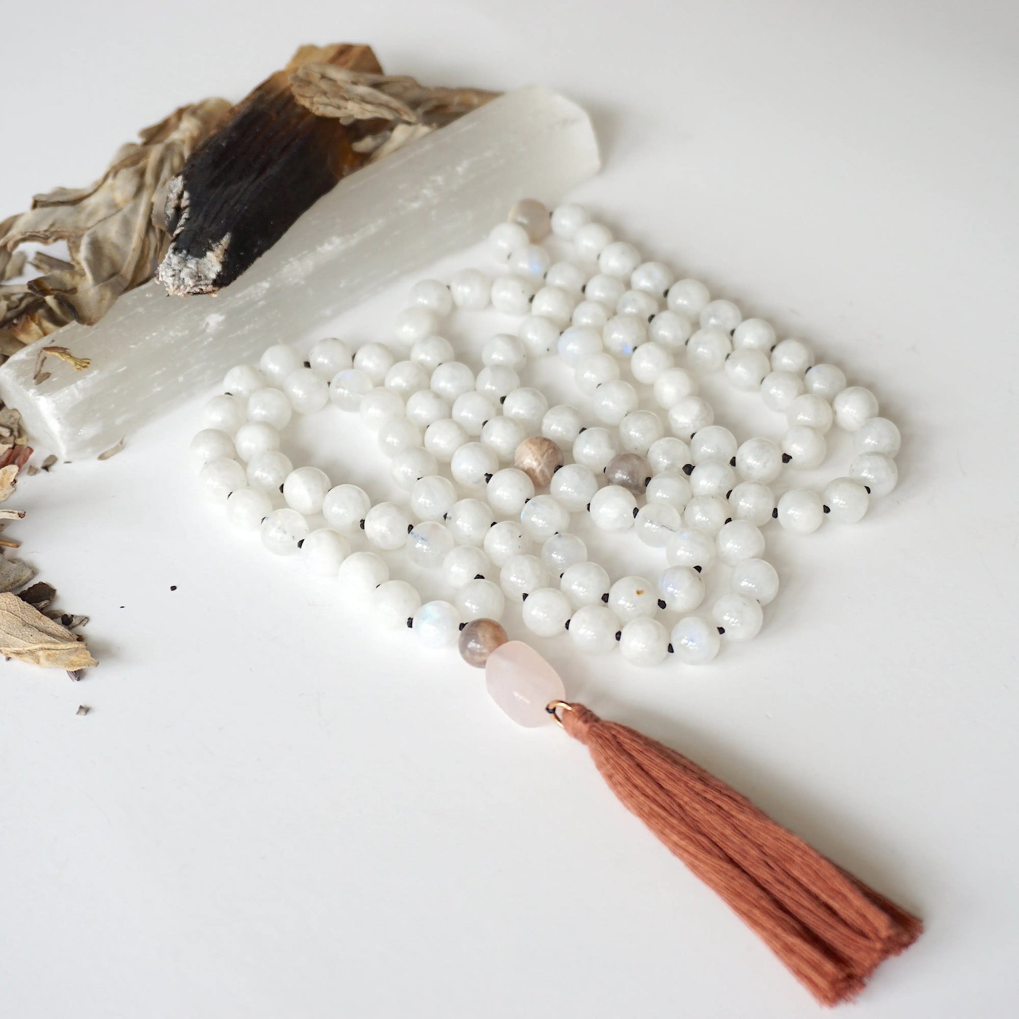 Detailed view of rainbow moonstone and moonstone bead mala necklace featuring 108 beads, rose quartz guru stone, and earthy brown tassel.