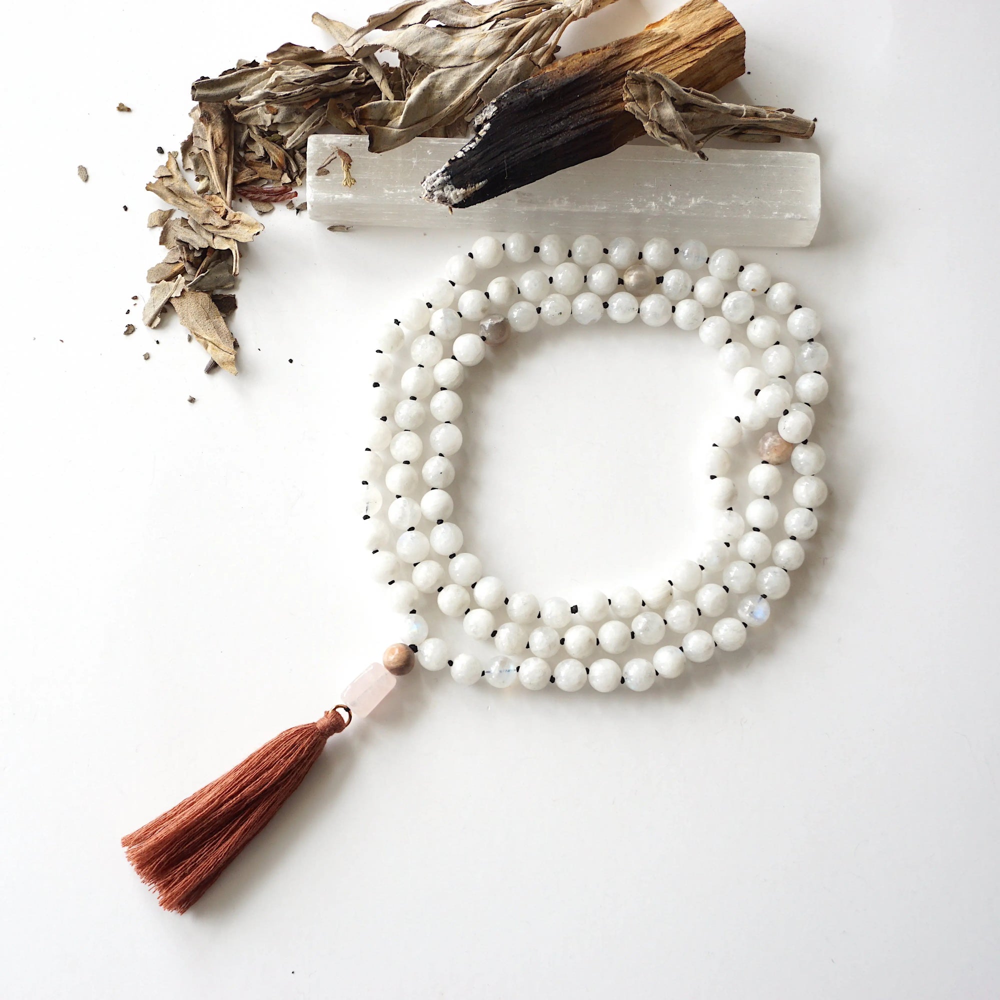 Top view of 108 bead rainbow moonstone mala necklace with rose quartz guru stone and earthy brown tassel, knotted silk cord design.