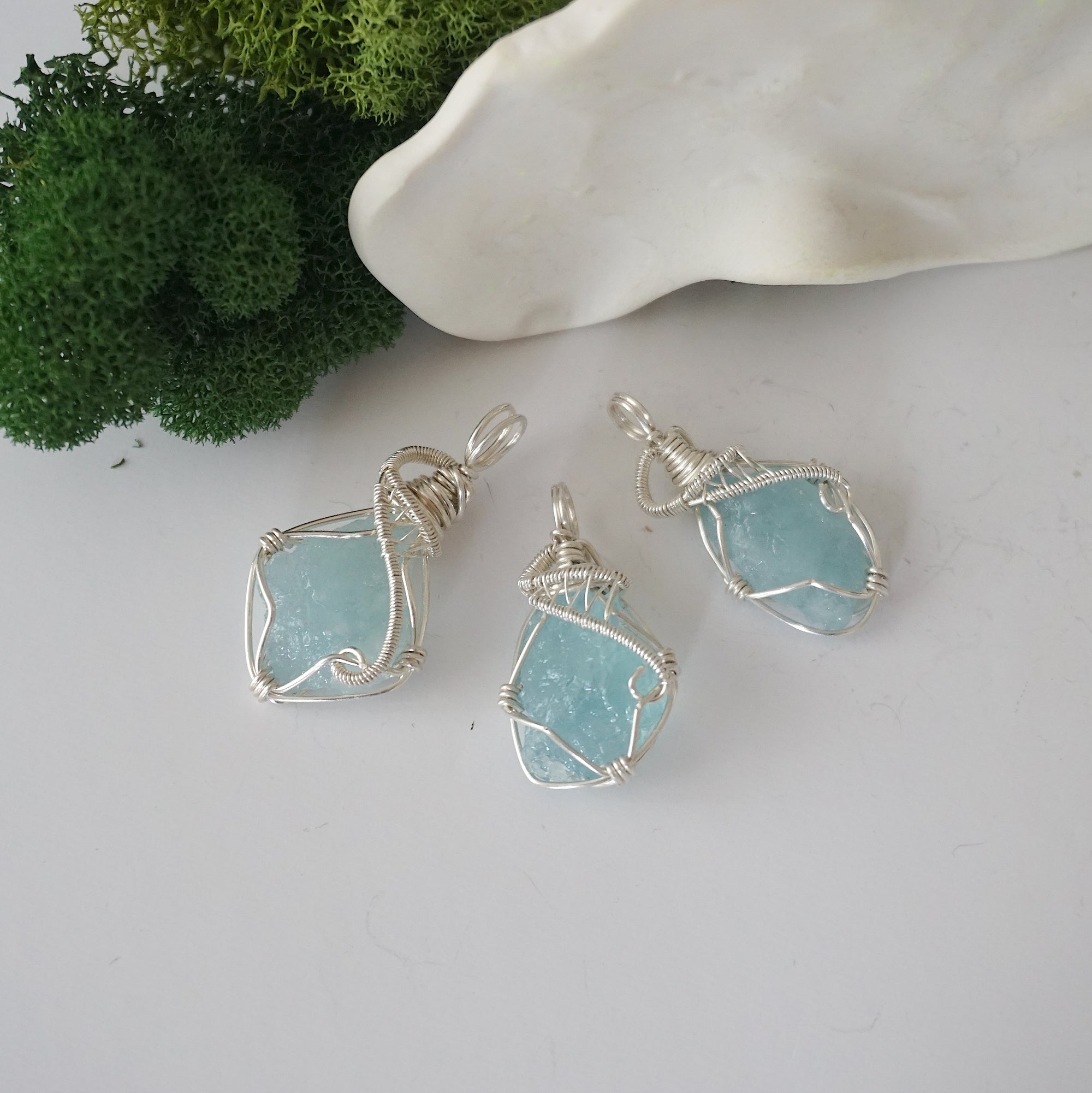 Three raw aquamarine pendants showing natural variation in stone size, shape, and pale blue tone — each one of a kind, March birthstone, 925 sterling silver wire wrapped, Designs by Nature Gems