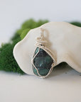 Front view of natural polished-raw emerald pendant with detailed artisan wire wrapping in soft silver copper.