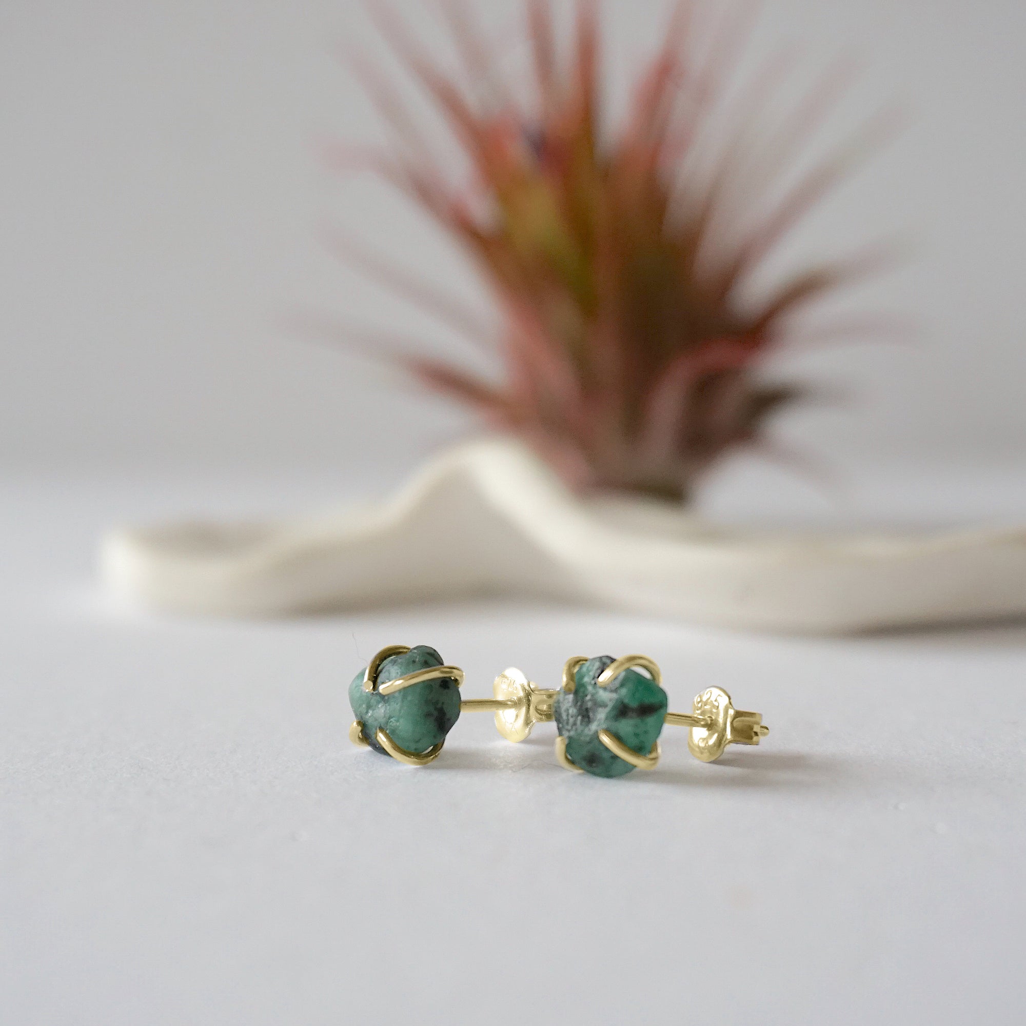 Raw emerald stud earrings in 14k gold vermeil at a slight angle showing natural green emerald and minimalist prong setting