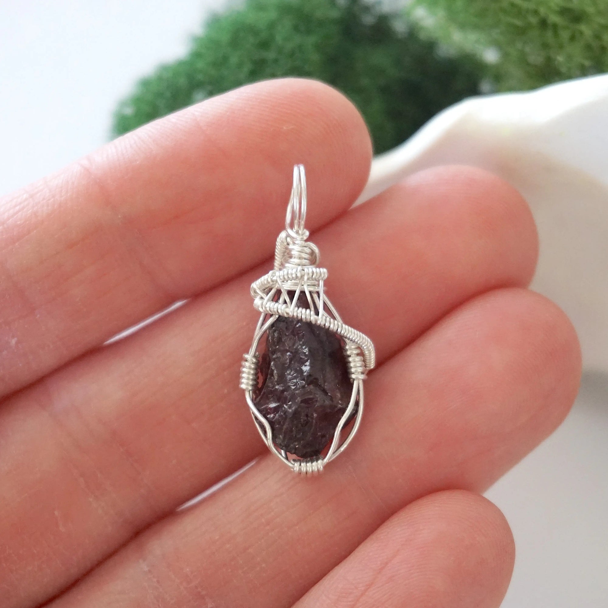 Raw garnet crystal pendant wire wrapped in sterling silver held in hand showing size