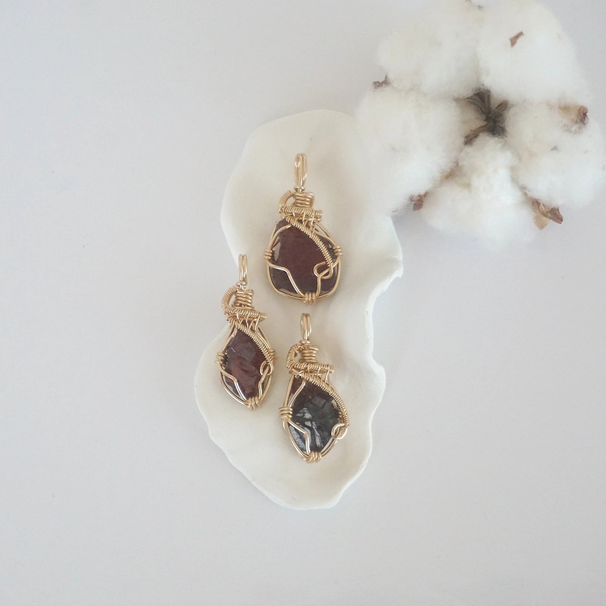 Three raw garnet pendants in 14k gold filled, showing natural variation in size, shape, and color. Handcrafted January birthstone jewelry by Designs by Nature Gems.