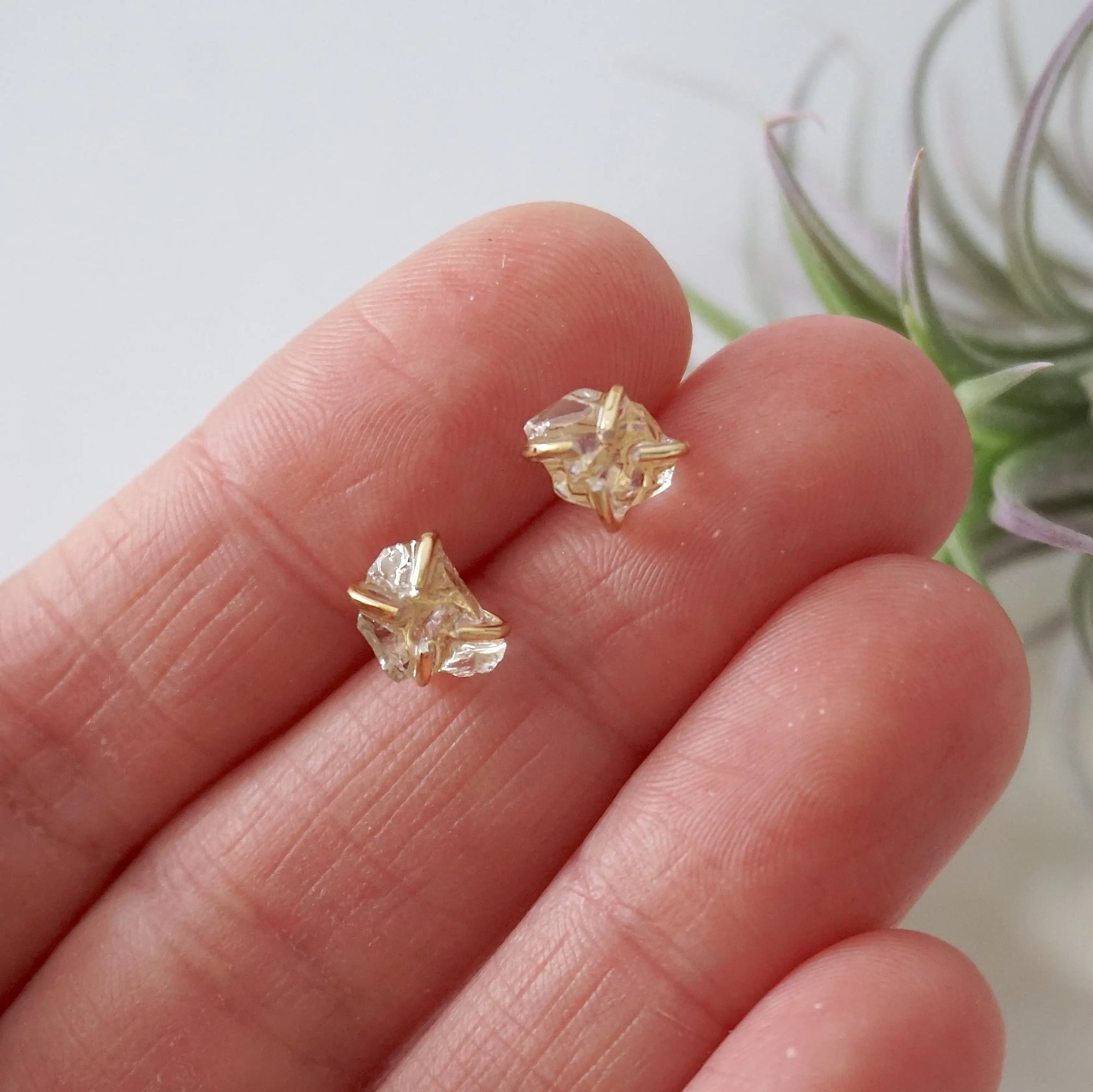 Raw Herkimer diamond stud earrings shown in hand for size reference in 14k gold vermeil prong settings.