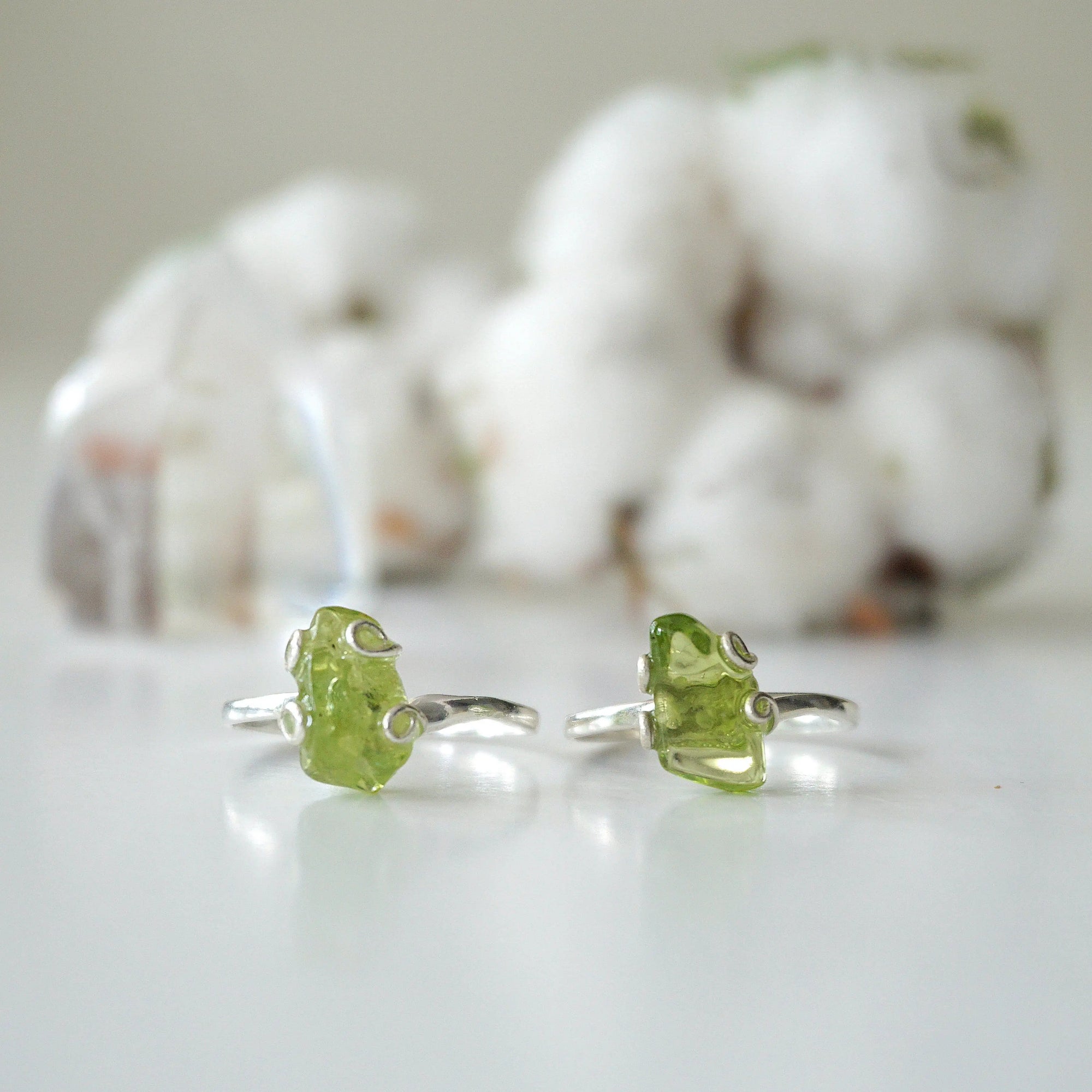 Two raw peridot adjustable rings showing natural variation in stone size, shape, and olive green colour — handcrafted 925 sterling silver August birthstone crystal rings for women