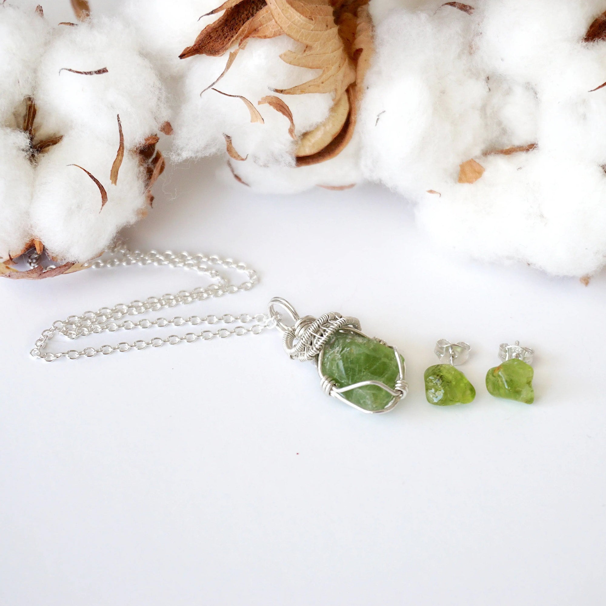 Raw peridot necklace and stud earring set for women on flat surface — 925 sterling silver chain and wire wrapped pendant with matching earrings, August birthstone crystal jewelry