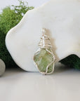 Detailed front angle view of simple raw peridot pendant in silver wire
