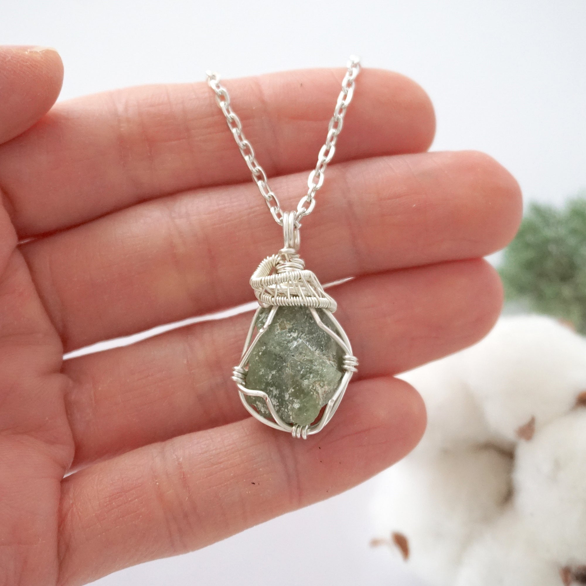 Handmade raw peridot pendant held in hand showing size — natural green peridot stone wire wrapped in silver finish, 10-20 carats, one of a kind, August birthstone