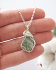 Handmade raw peridot pendant held in hand showing size — natural green peridot stone wire wrapped in silver finish, 10-20 carats, one of a kind, August birthstone