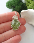Handmade raw peridot pendant held in hand showing size — natural green peridot stone wire wrapped in 925 sterling silver, approx. 1 inch, one of a kind
