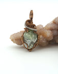 Front view of raw peridot pendant for women — soft sage olive green crystal with natural surface texture, antique bronze and dark silver wire wrap, handcrafted August birthstone jewelry