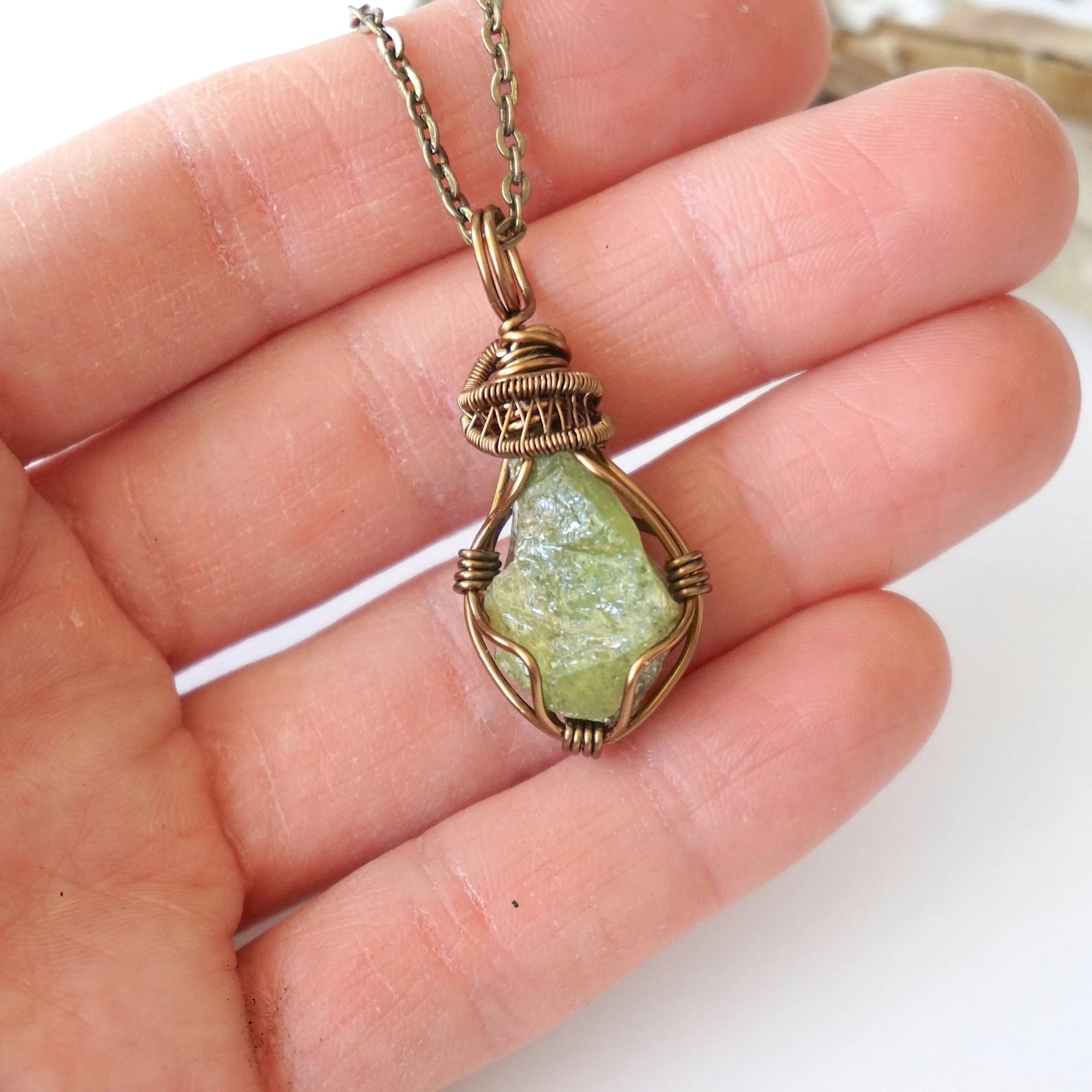 Raw peridot pendant for women held in hand for size reference — natural olive green crystal in antique bronze wire wrap, handcrafted August birthstone jewelry