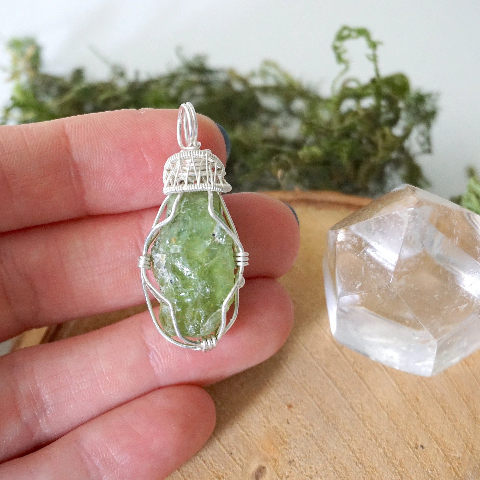 Raw peridot pendant for women held in hand for size reference — natural olive green crystal in 925 sterling silver wire wrap, handcrafted August birthstone jewelry