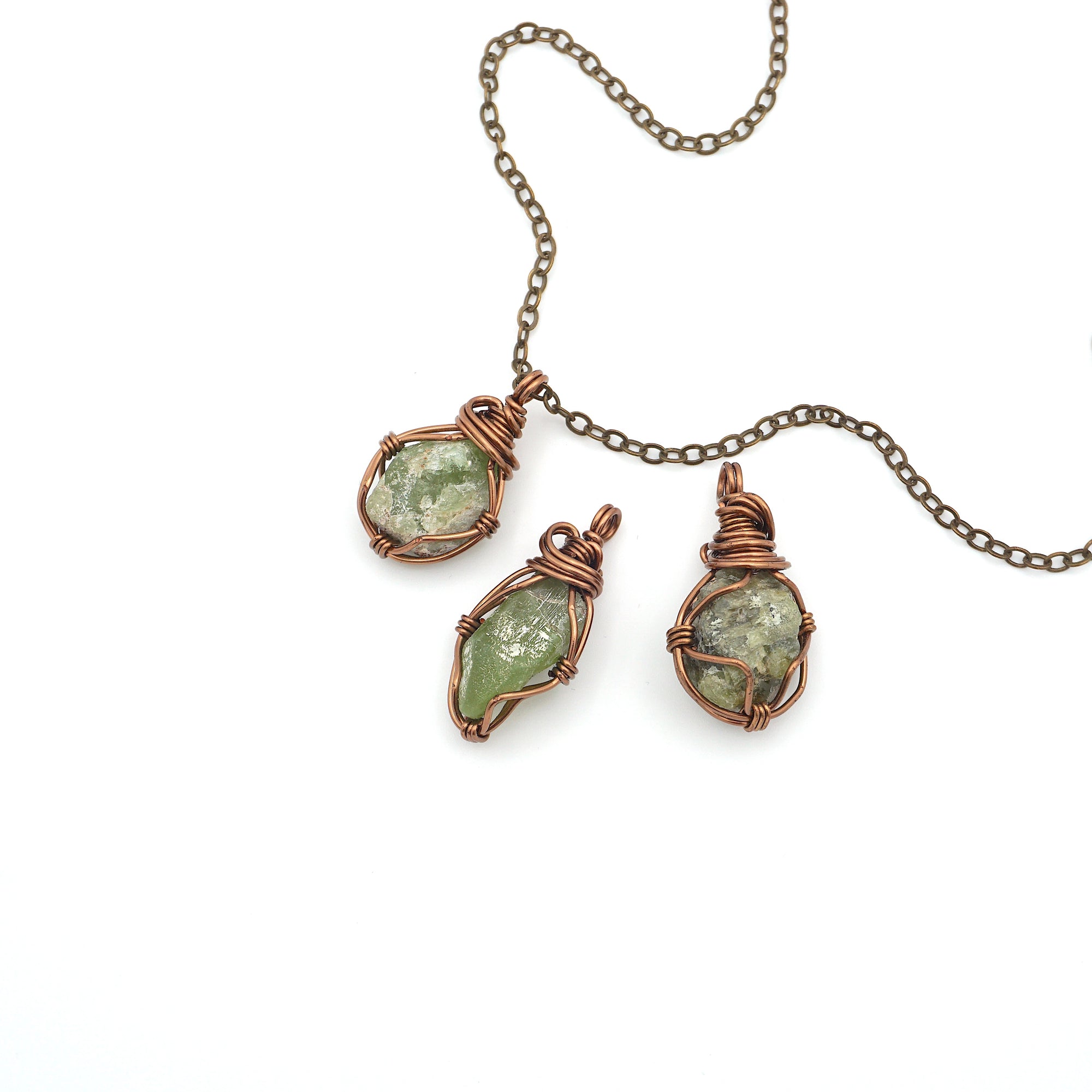 Three raw peridot pendants showing natural variation in size, shape, and olive green colour — handcrafted wire wrapped August birthstone necklaces