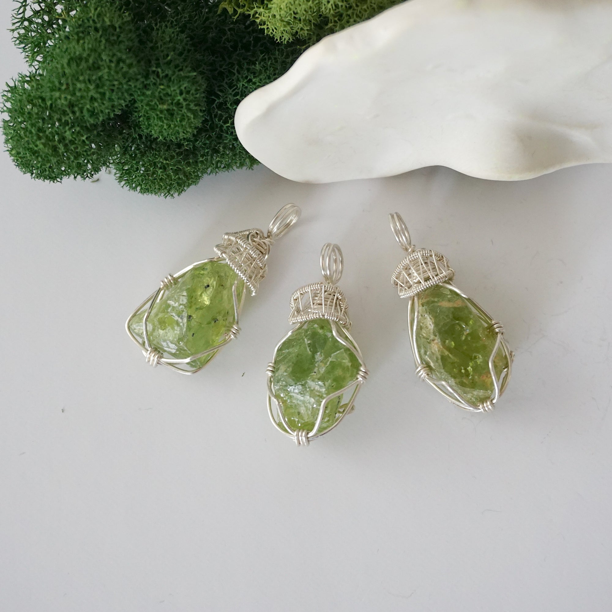 Three raw peridot pendants showing natural variation in stone size, shape, and green colour — each one of a kind, August birthstone, 925 sterling silver wire wrapped, Designs by Nature Gems