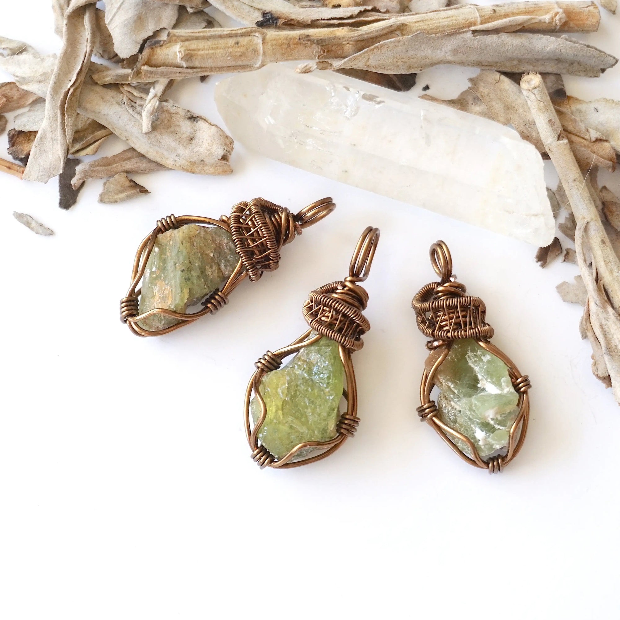 Three raw peridot pendants for women showing natural variation in size, shape, and olive green colour — handcrafted antique bronze wire wrapped August birthstone necklaces