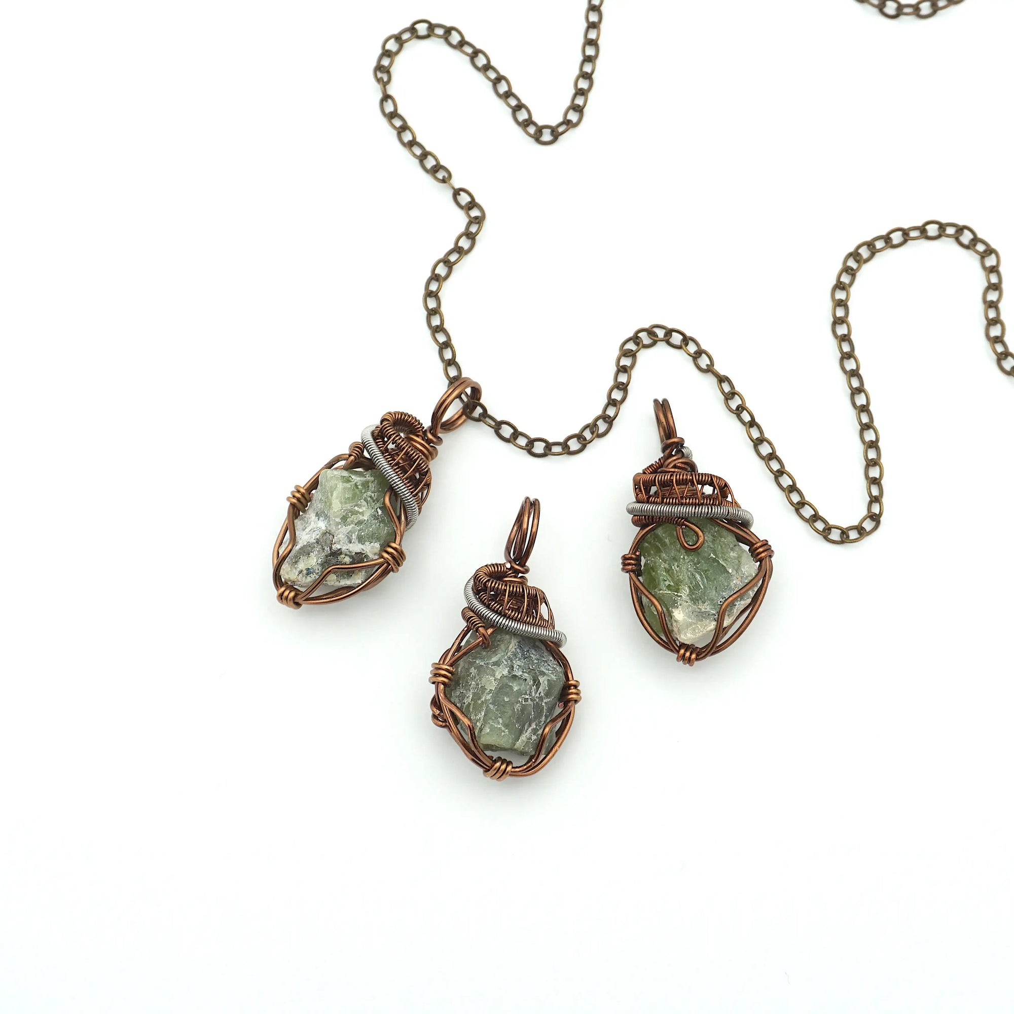 Three raw peridot pendants for women showing natural variation in size, shape, and olive green colour — handcrafted two-tone wire wrapped August birthstone necklaces