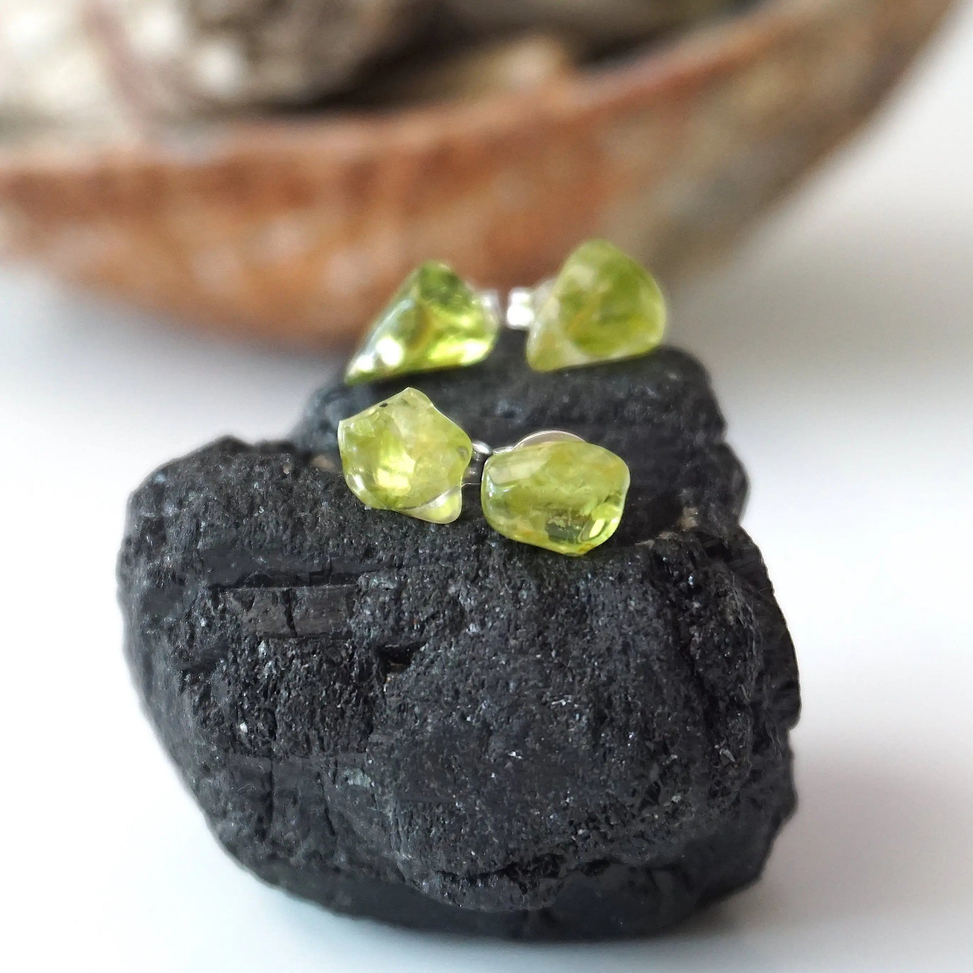 Two pairs of raw peridot stud earrings showing natural variation in stone shape, size, and olive green colour — handcrafted 925 sterling silver August birthstone crystal studs by Designs by Nature Gems