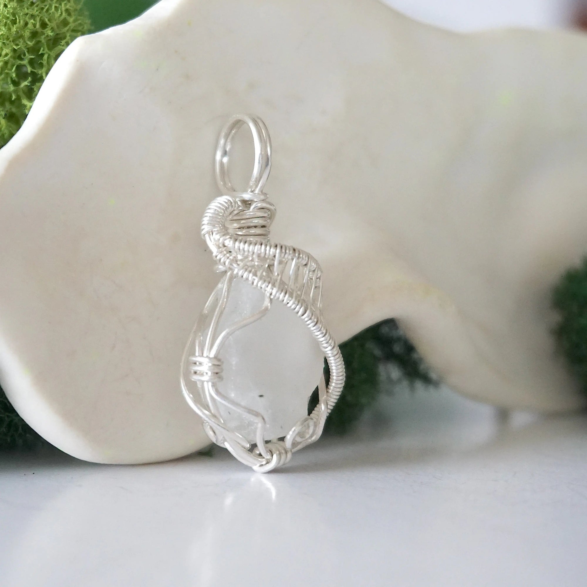 Side angle of raw rainbow moonstone pendant showing artisan wire wrapped sterling silver detail