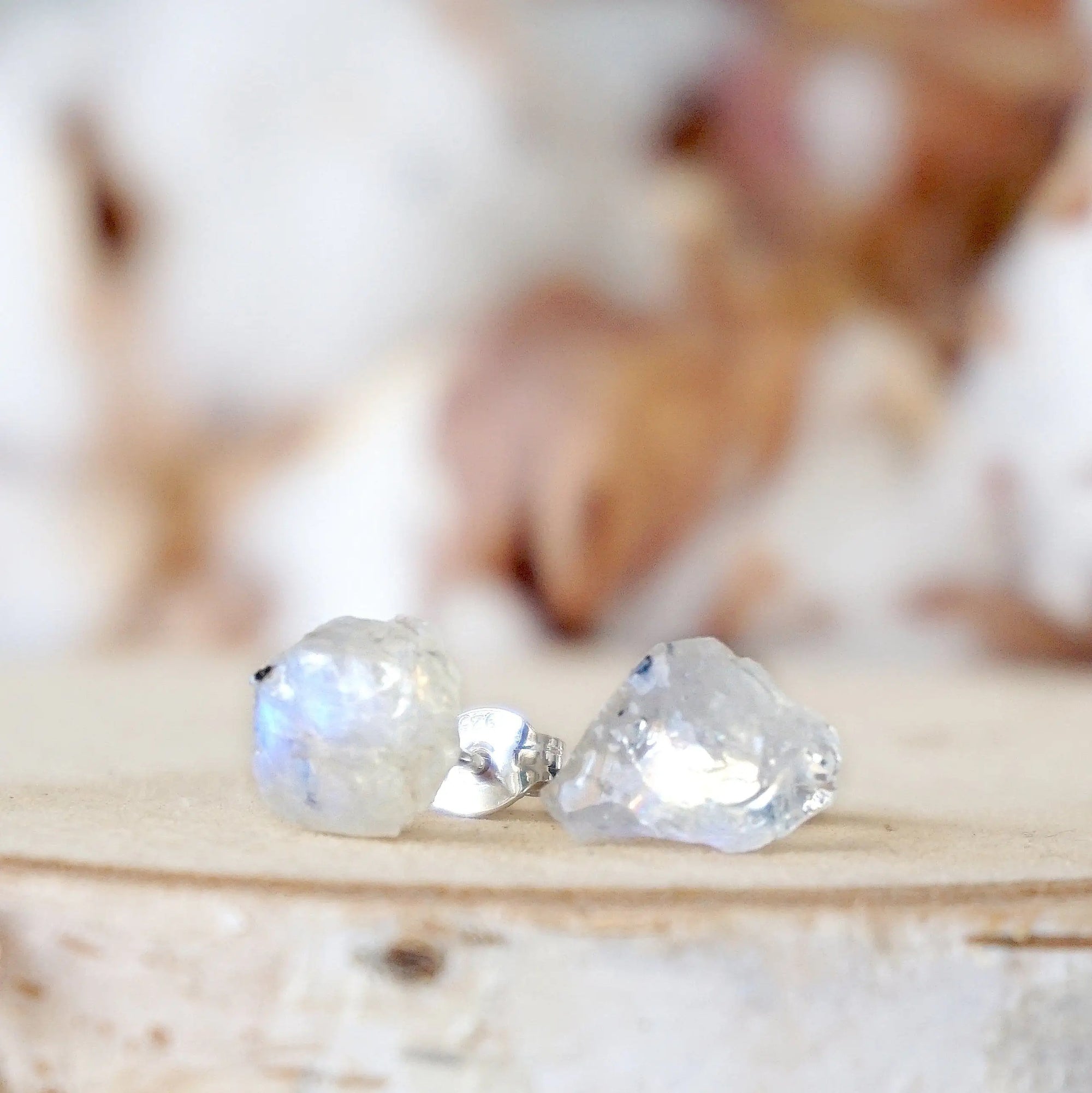 Left angle close-up of raw rainbow moonstone stud earrings showing natural variation in uncut moonstone and subtle flash, June birthstone.