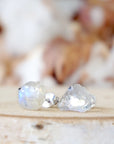 Left angle close-up of raw rainbow moonstone stud earrings showing natural variation in uncut moonstone and subtle flash, June birthstone.