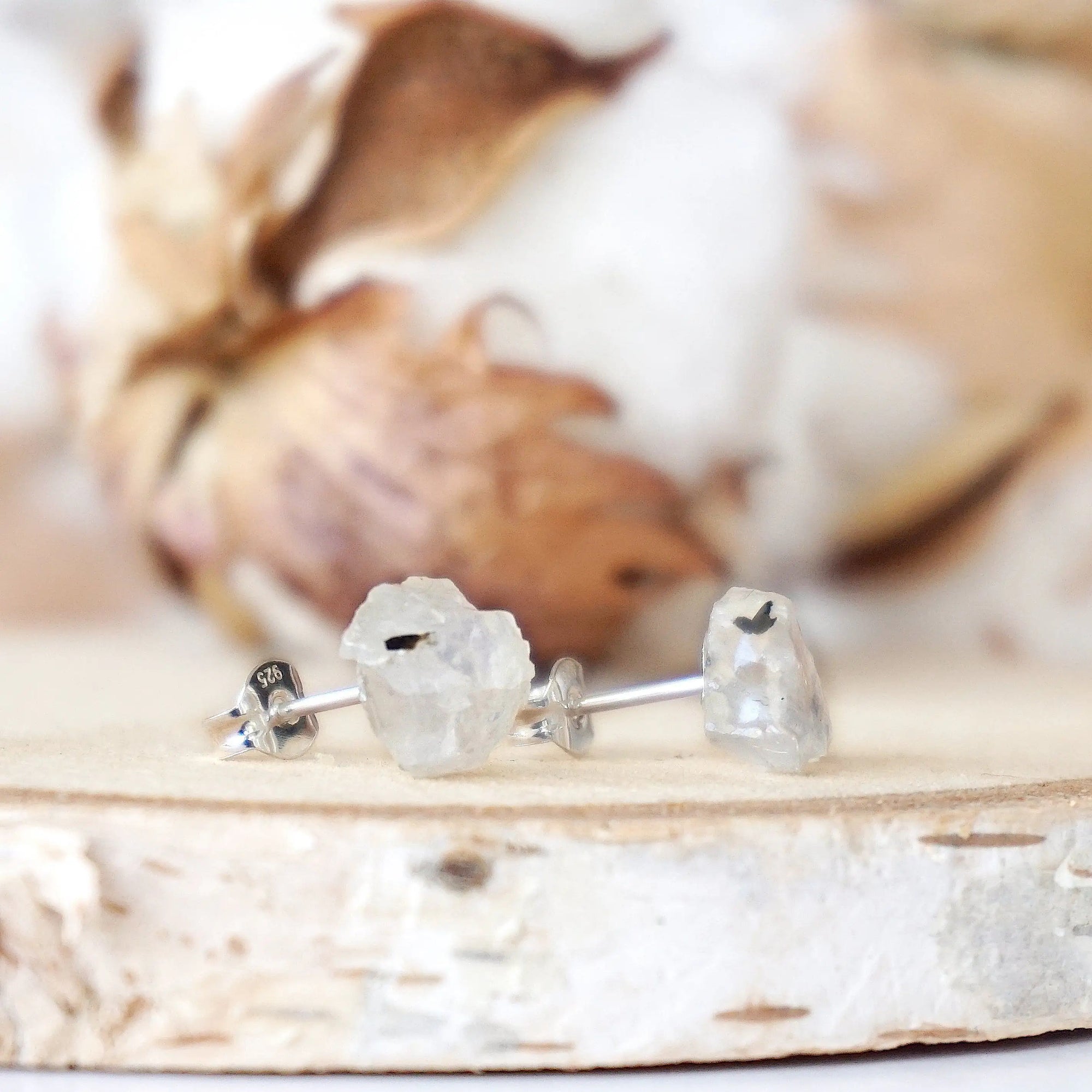 Right angle close-up of raw rainbow moonstone stud earrings highlighting organic stone shape and minimalist sterling silver post setting.