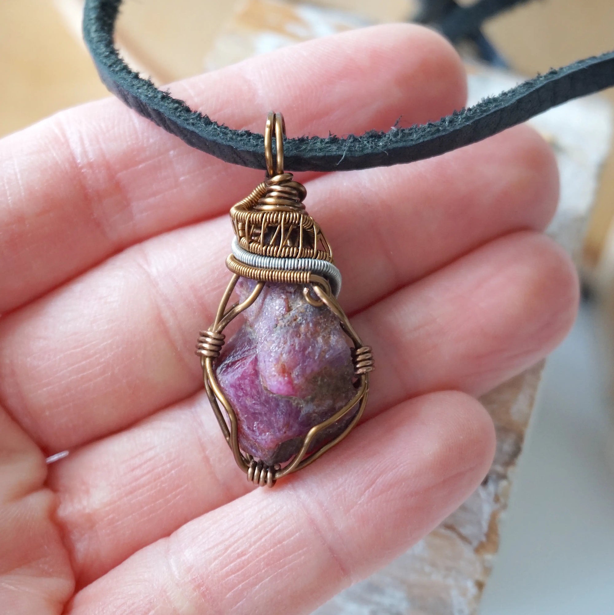 Raw ruby pendant held in hand to show size — natural ruby stone in two-tone bronze and silver wire wrapping, men's handmade crystal necklace