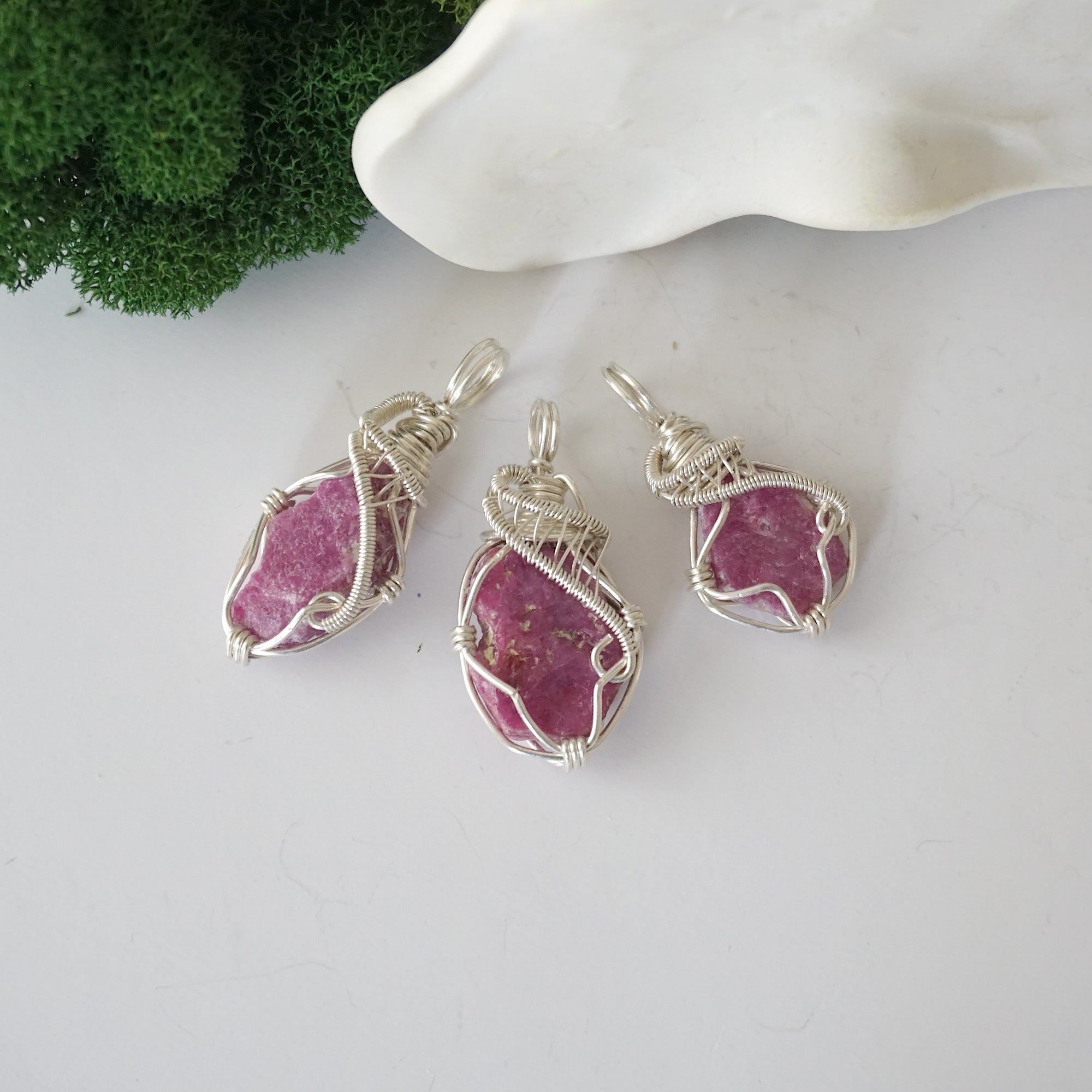 Three raw ruby pendants showing natural variation in stone size, shape, and pink colour — each one of a kind, July birthstone, 925 sterling silver wire wrapped, Designs by Nature Gems