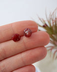 Raw ruby stud earrings held in hand to show size — natural rough ruby stones on 925 sterling silver posts, July birthstone earrings