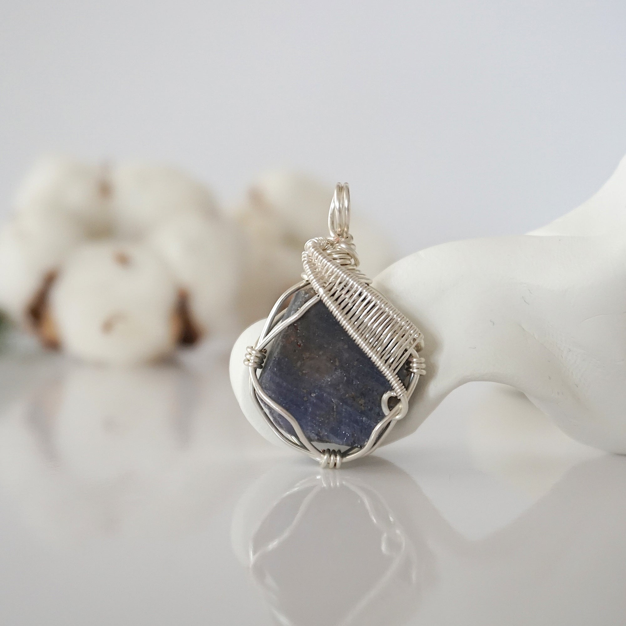 Front view of raw sapphire pendant — natural unpolished dark blue corundum stone hand-wrapped in detailed silver finish wire, handcrafted artisan crystal jewelry